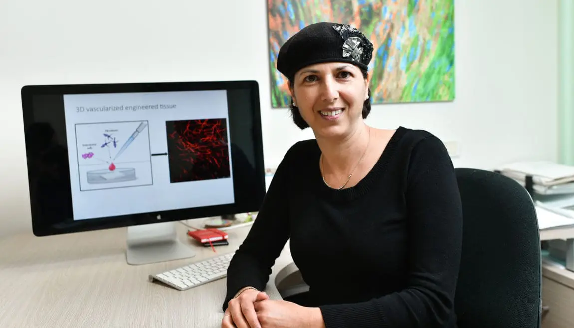 technion professor shulamit levenberg, cultivated meat entrepreneur, sitting in front of a desktop computer in an office wearing black sweater and black beret | Donate to Technion Israel | Support the Technion University | American Technion Society