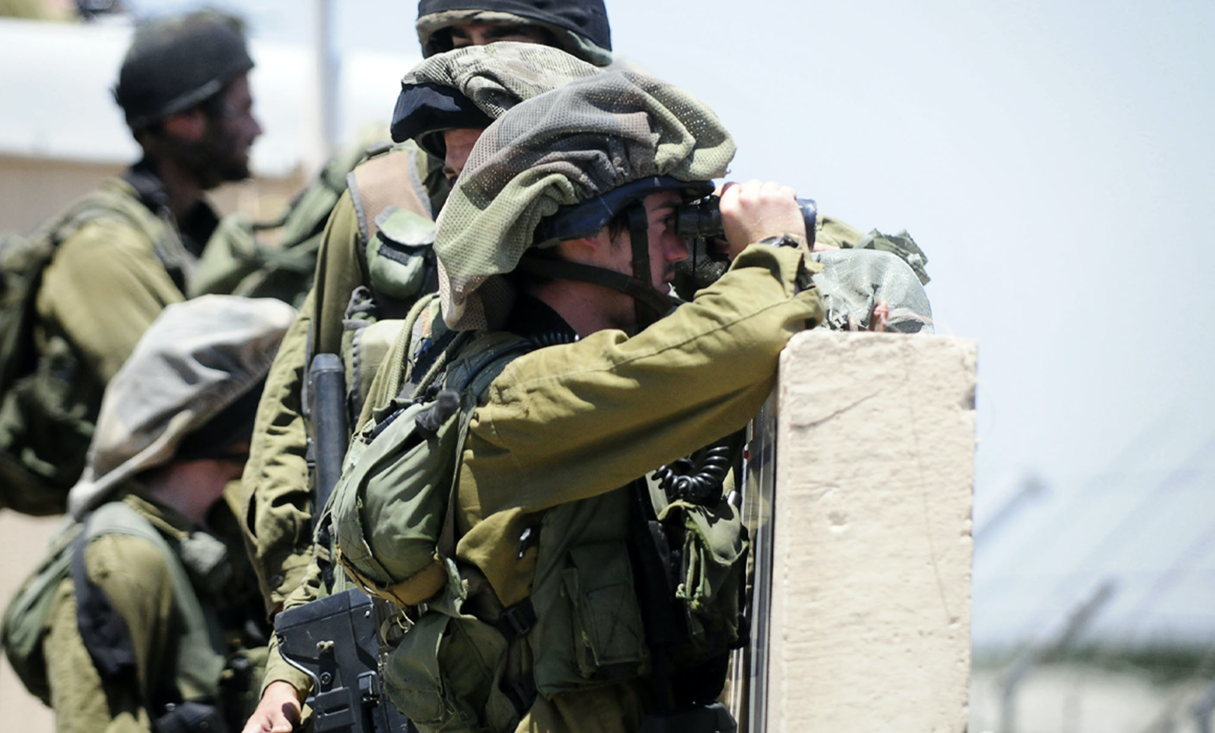 IDF soldiers behind a barrier looking through binoculars