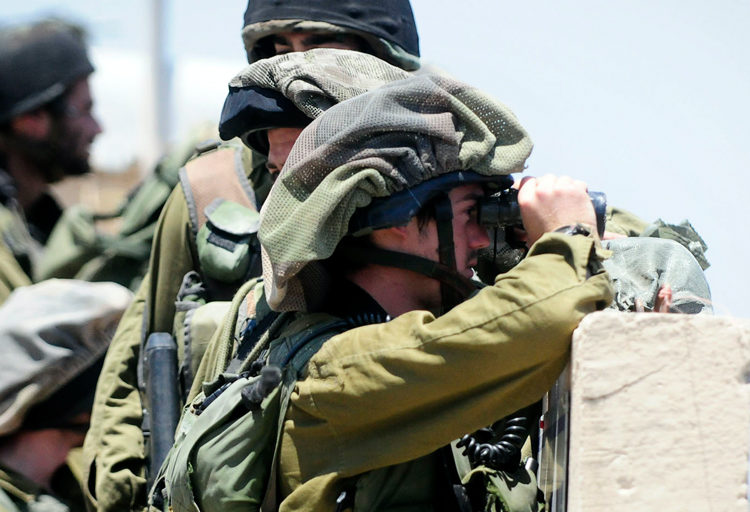 IDF soldiers behind a barrier looking through binoculars