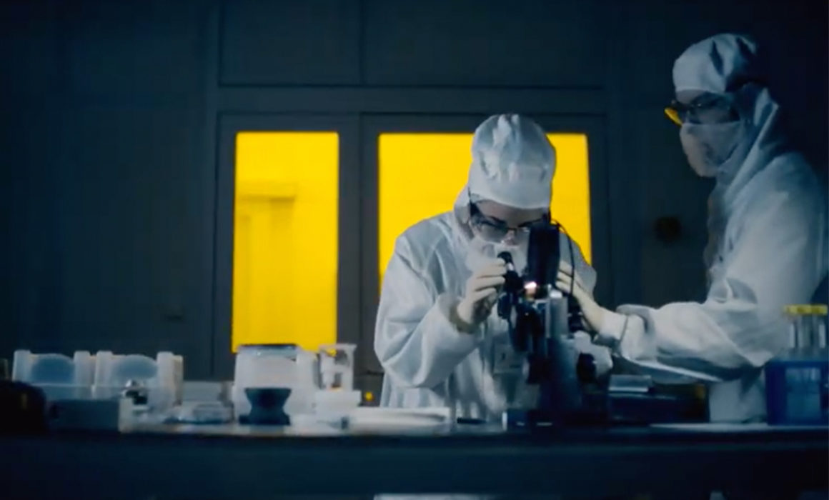 Two researchers in protective gowns working in a Technion lab with microscopes.