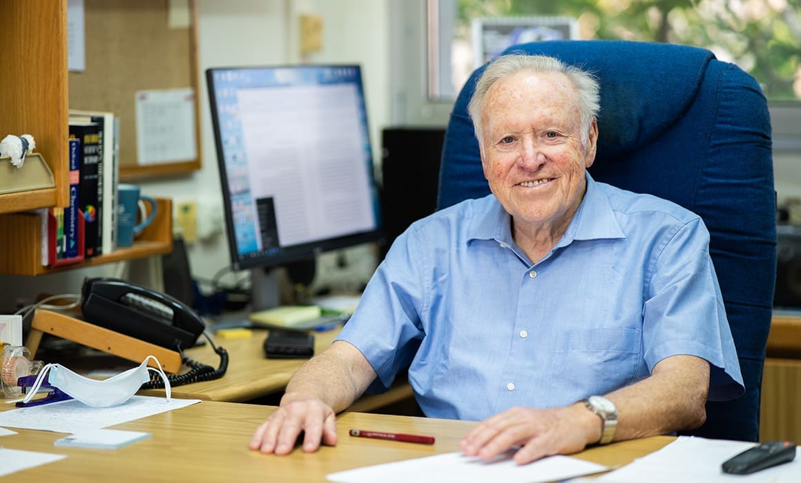 Distinguished Professor Yitzhak Apeloig at a desk in a blue chair | Donate to Support Israel | Technion University