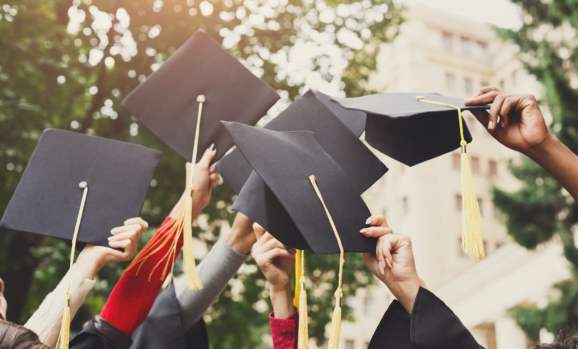 technion graduates holding up their black Ph.D. graduation caps with yellow tassels with buildings and trees in the background | Donate to Support Israel | Technion University