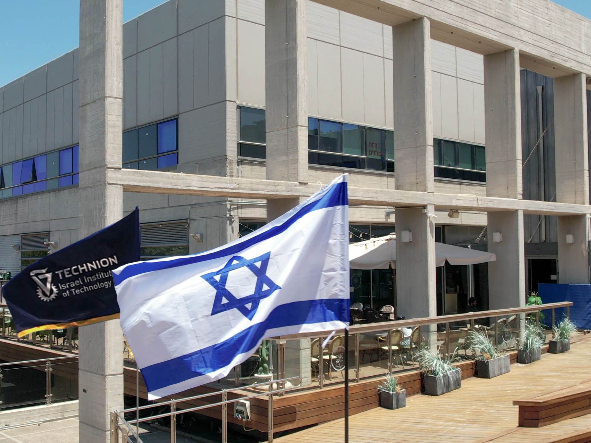 israeli flag and Technion - Israel Institute of Technology flag in front of a grey building on the Technion campus | American Technion Society | Donate to Israel