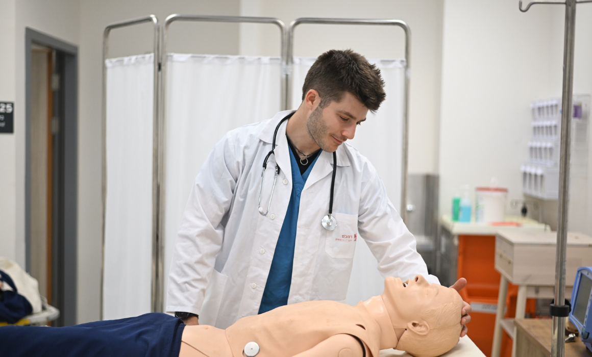 Student in lab coat treating medical manikin.