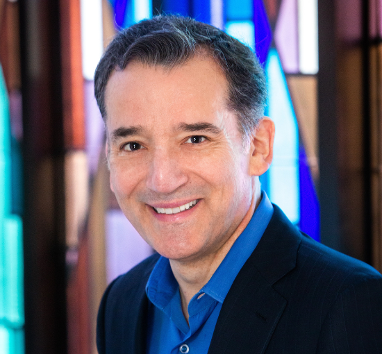 A headshot of a man wearing a suit and blue shirt