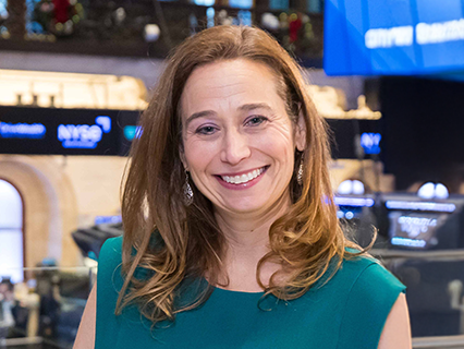Women standing at the NYSE with shoulder length hair and a team sleeveless top.