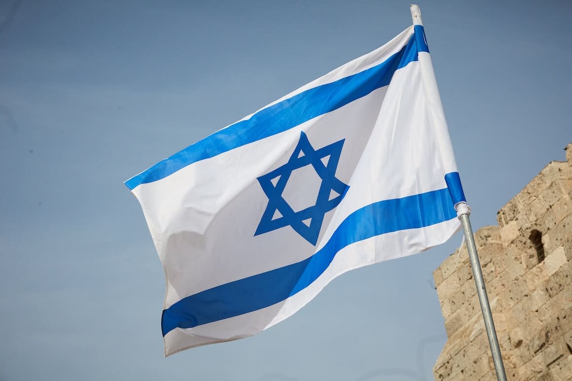 israeli flag flying in wind with stone building in background | Donate to Support the Technion University | American Technion Society
