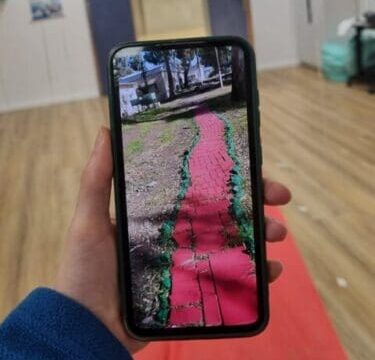 red carpet laid out in hospital with green balloons on either side. phone in front of carpet holding up a photo of the trail recreated
