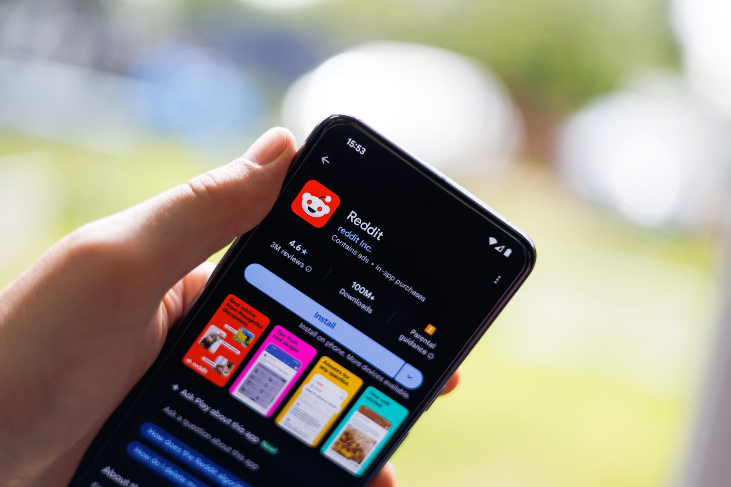 hand holding smartphone with Reddit being downloaded in front of blurred nature background