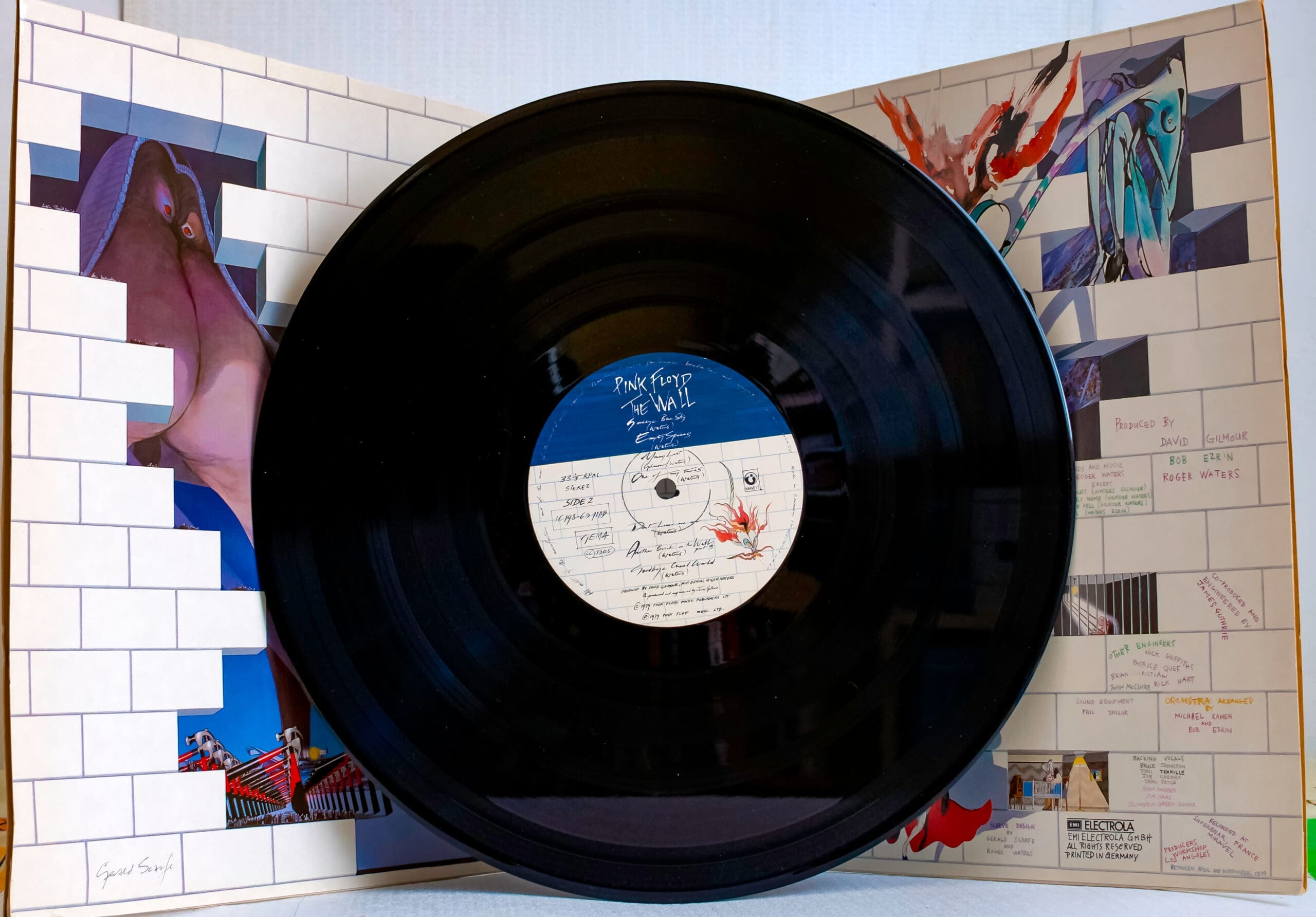 Pink floyd record in front of psychadelic brick wall background.