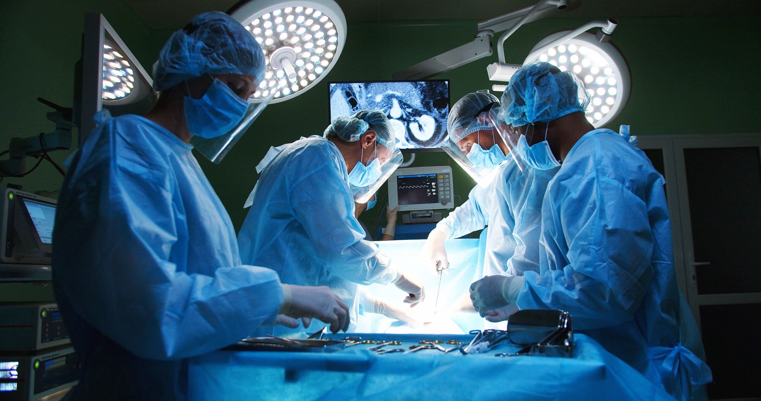 four surgeons in full scrubs stand around operating table
