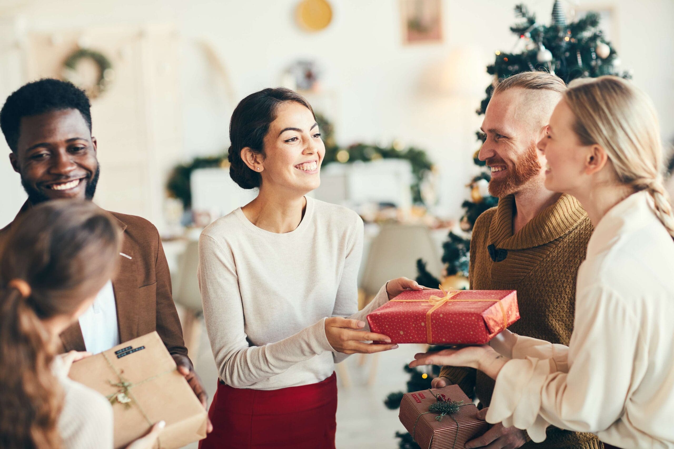 group of smiling adults standing in a circle exchanging gifts. festive holiday decor in the background.