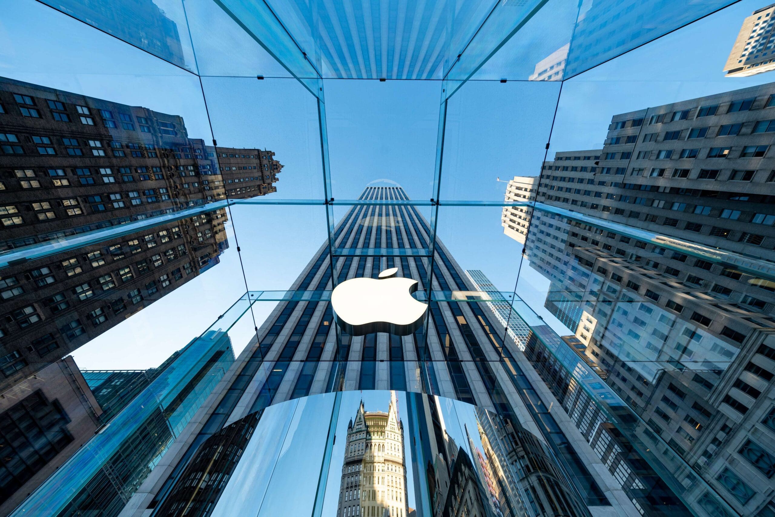 view from ground level looking up at Apple Store 5th Ave in NYC. Skyscraper in the background.