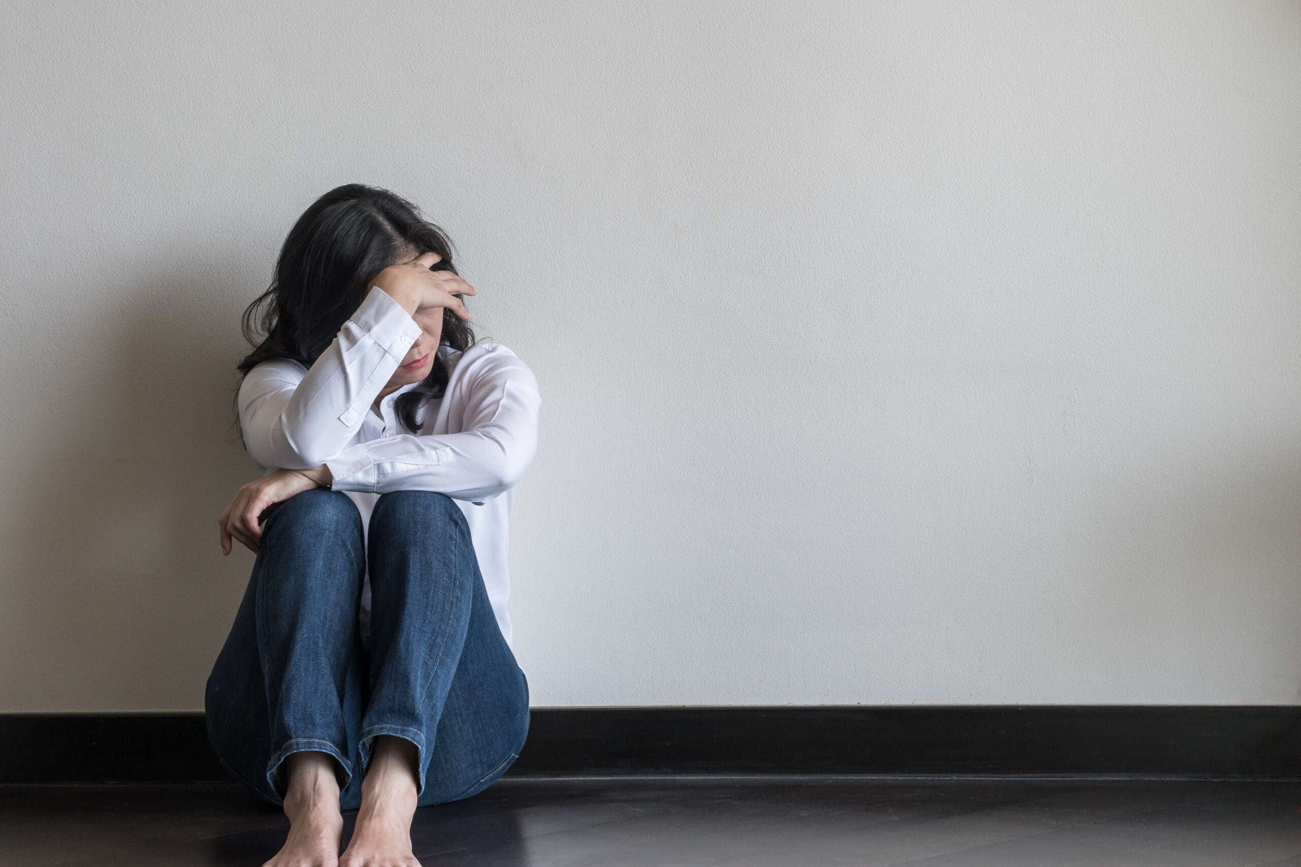 technology abuse | woman with headache or migraine sitting back against wall on the floor in domestic home | American Technion Society